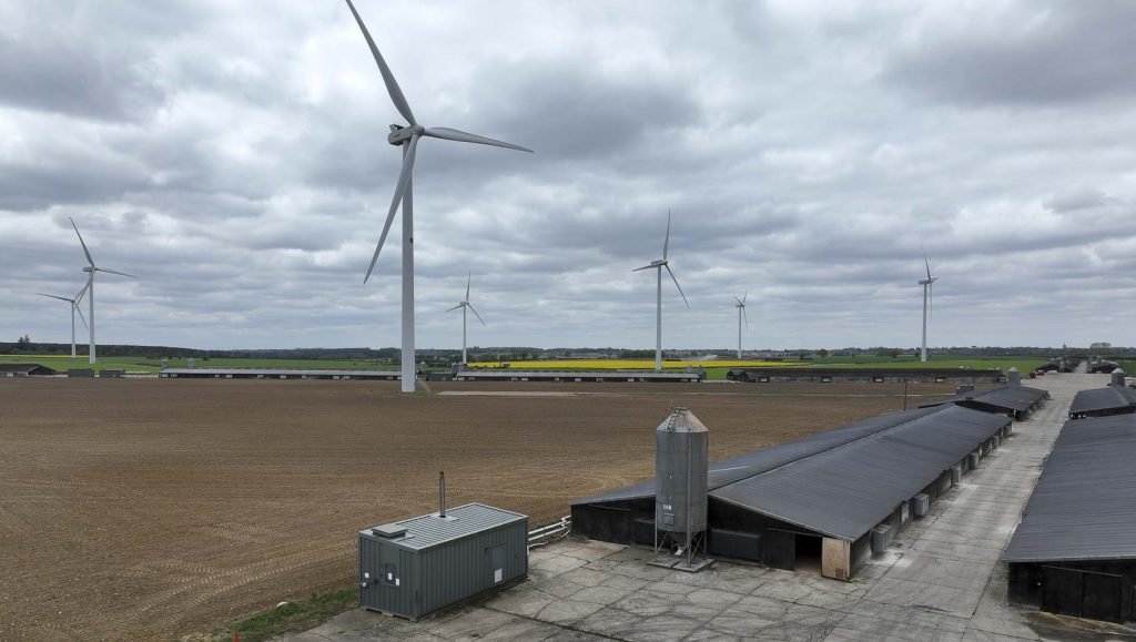 Landscape photo of grey barns in front of wind turbines