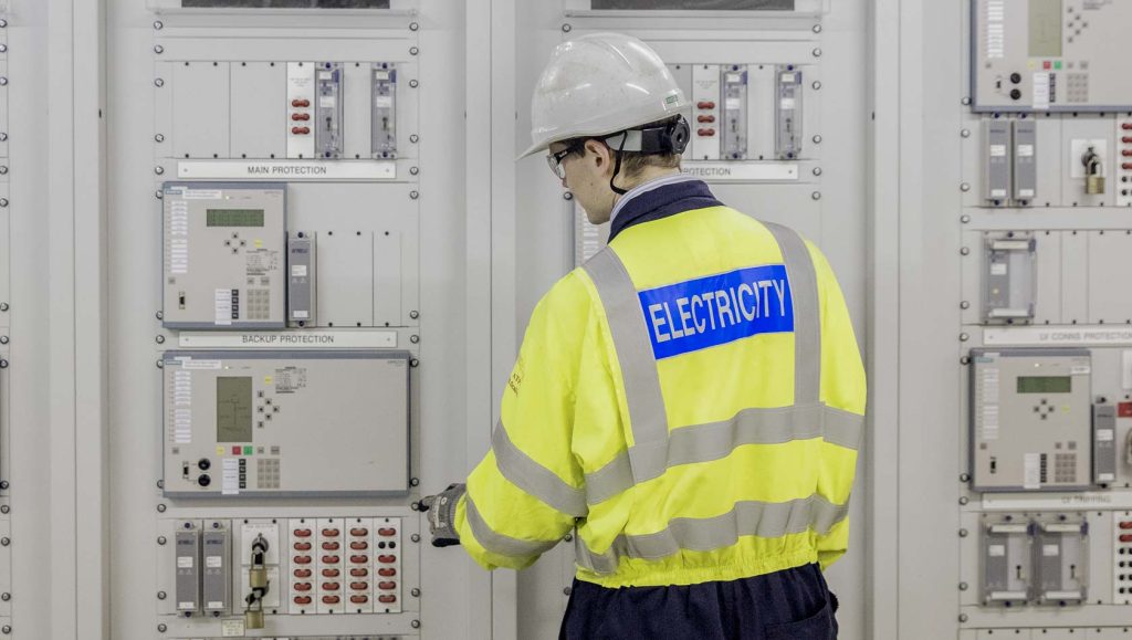 A person in a high vis jacket in front of an electric panel