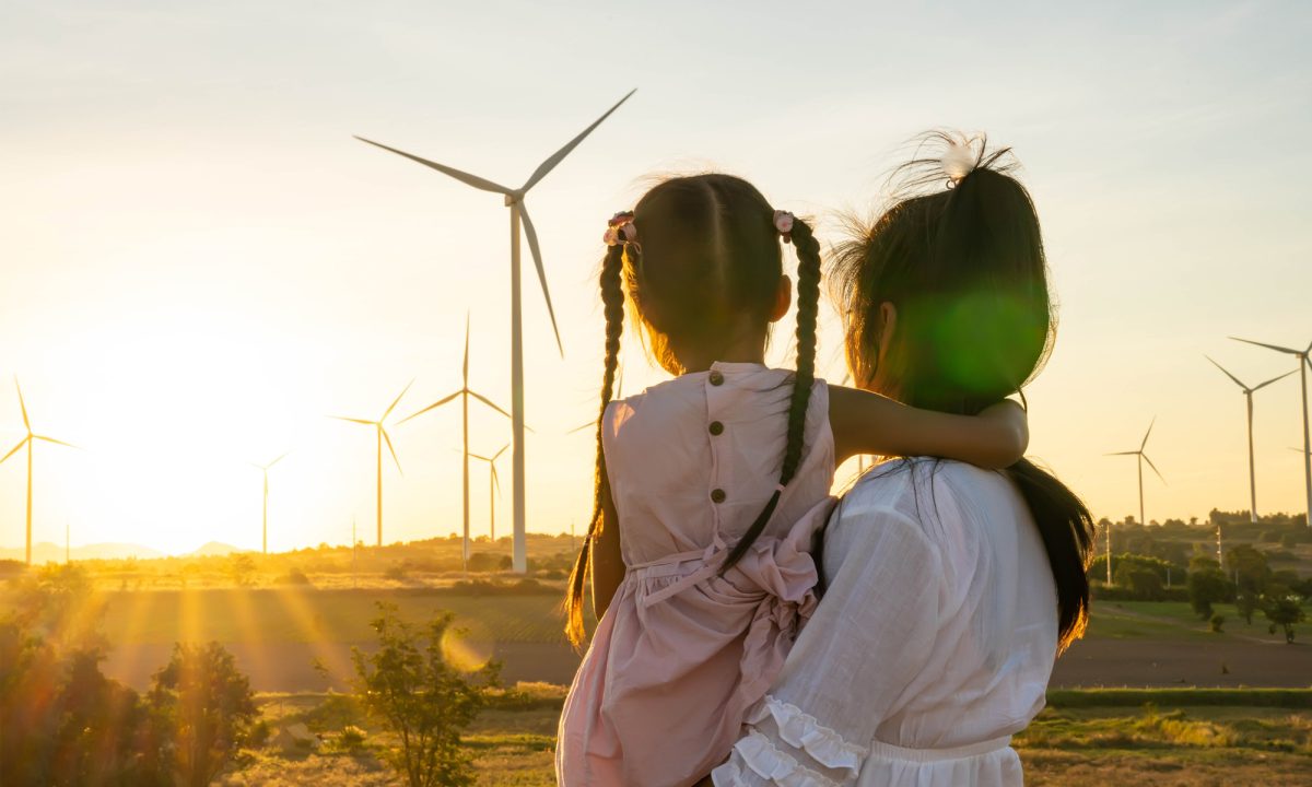 A woman holds a girl and they look at wind turbines