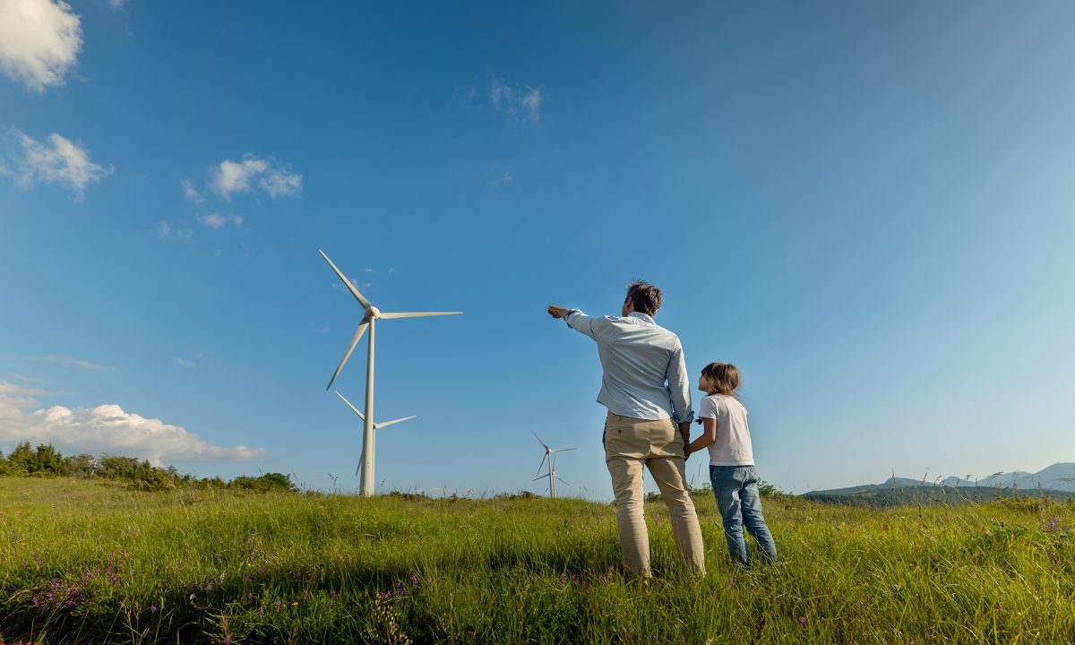 A man holds a childs hand and points at a wind turbine
